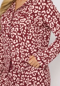 Bordeaux pyjama set met een roze abstracte luipaardprint. Bestaat uit een overhemd met knopen, een borstzak en lange mouwen met omgeslagen manchetten.