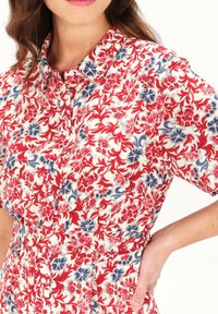 Bloemprint shirt met een witte achtergrond en rode en blauwe patronen, korte mouwen en een button-down kraag, gemaakt van lichtgewicht stof.