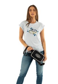 Une chemise courte à manches bleues claires présente un motif floral avec le "17" et des paillettes. Un jean bleu foncé et un sac en bandoulière noir avec des finitions blanches.