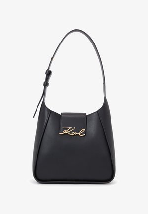 Svart läderhandväska med en böjd form, en kort rem och en guldlogotyp på framsidan. Sleek yta, minimalistisk design.