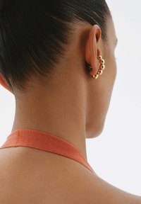 Pendientes de aro de oro con cuentas redondeadas de diferentes tamaños, situados sobre un fondo de piel suave con una cinta naranja en el cuello.