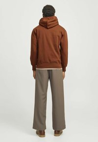 Brun hætte sweatshirt med en stor justerbar hætte, der har en afslappet pasform. Sammen med lysebrune vide bukser og brune sko.