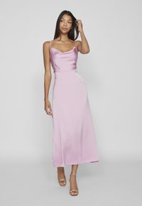 Rosa satängmaxiklänning med hängande halsringning och tunna axelband, med en flödande silhuett som når mitt på vaden; mjuk textur.