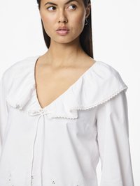 Bluză albă cu guler ruffles lat, detaliu cu fundă și accente florale brodate la margine. Mâneci lungi și material din bumbac ușor.