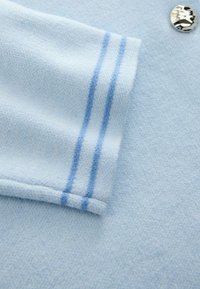 Jasnoniebieska tkanina o miękkiej fakturze, z dwutonowym paskowanym wzorem w ciemniejszym odcieniu niebieskiego oraz błyszczącym, metalicznym guzikiem jako akcentem.