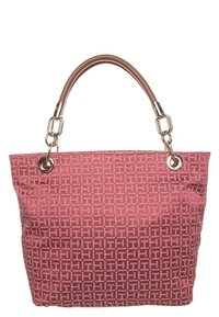 Sac fourre-tout rouge avec un motif géométrique blanc à répétition et des poignées marron fixées par des anneaux et des fermoirs en métal doré.