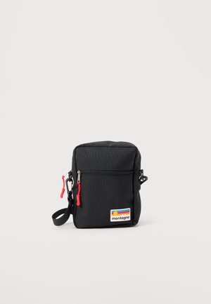 Crna pravokutna torba preko tijela s prednjim džepom na patentni zatvarač, crvenim metalnim klizačima patenta i šarenim logotipom "montagne" u donjem desnom kutu.