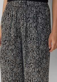 Zwart-witte gestreepte broek met geometrische ontwerpen, elastische tailleband en lichtgewicht stof. Close-up toont ingewikkelde details.