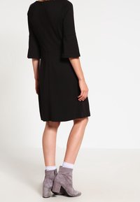 Czarna sukienka z rękawami dzwonami i suwakiem z tyłu, połączona z szarymi botkami sięgającymi kostek na słupkowym obcasie. Gładka tkanina i długość do kolan.