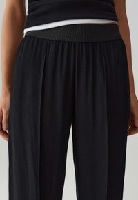 Pantaloni neri a gamba larga con un tessuto testurizzato e una cintura elastica. Il design presenta pieghe sottili per un aspetto fluido.
