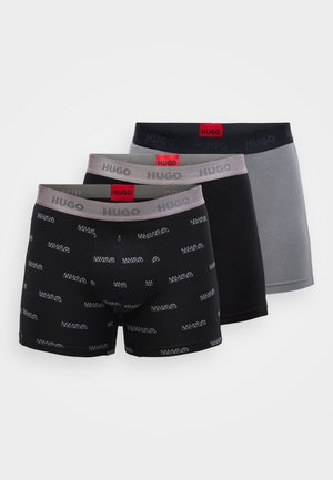 Trys trumpų dėvėti šortų poros įvairiomis spalvomis: juodi su logotipo raštu, vieni juodi ir pilki, su elastingais juosmenimis, kuriuose yra logotipo detalės.