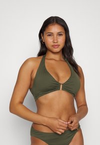 Alyvuogių spalvos bikinis, kuriame yra viršus su surinkta apdaila ir auksinėmis detalėmis, derinamas su atitinkamomis žemomis kelnaitėmis.