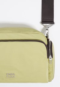 Padded, light green crossbody bag with a brown zipper, silver hardware, and an adjustable strap. Features logo "BIMBA Y LOLA" prominently.
