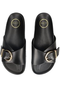 Černé skluzné sandály s širokým křížovým popruhem a zlatou sponou. Vyrobené z hladké kůže s plochou podrážkou, s logem značky.