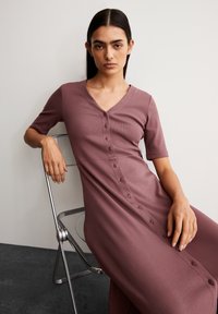 V-neck, short-sleeve dress in mauve ribbed fabric featuring a button front design and a relaxed fit, layered over a smooth, flat surface.
