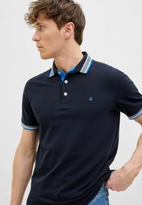 Marineblauwe polo met een klassieke kraag, contrasterende lichtblauwe en witte gestreepte afwerking, en drie knopen. Zachte stof, slim-fit ontwerp.