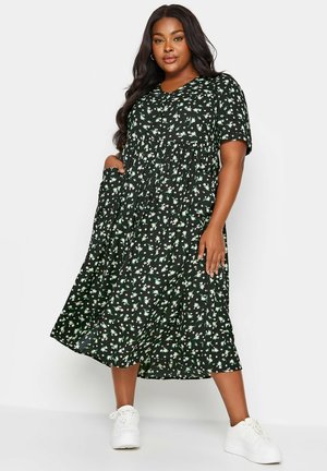 Schwarzes Blümchenkleid mit knielangem Saum, kurzen Ärmeln, gerafftem Taillenbereich und weißen Blumenmustern. Getragen mit weißen Turnschuhen.