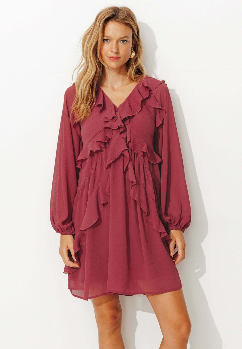 Robe en chiffon couleur framboise avec des manches longues, un décolleté en V, et des volants superposés sur le devant et les manches, offrant une coupe décontractée.