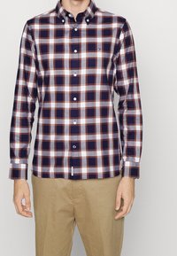 Camicia button-up con un motivo a quadri in navy, bianco e ruggine. Realizzata in cotone, con colletto e maniche lunghe. Bottoni sul davanti.