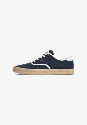 Marineblauer Canvas-Sneaker mit weißen Besätzen und Schnürsenkeln, gewebter beiger Sohle, niedrigem Design und kleinem Logo an der Seite.