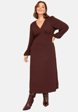 Rochie lungă burgundă cu suprafață texturată, decolteu adânc în V și mâneci bufante, asortată cu cizme maro până la genunchi.