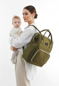 Olivgrön vadderad ryggsäck med dubbla topphandtag och justerbara axelremmar, med en framficka med dragkedja och logodetalj.