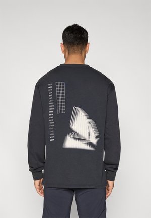 Camisa negra de manga larga con un diseño gráfico en la parte trasera que presenta formas iluminadas en blanco y un patrón de cuadrícula en azul en el lado izquierdo.