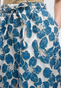 Μπλε και μπεζ παντελόνι με κορδόνι και λουλουδάτο σχέδιο, συνδυασμένο με καφέ τοπ, που δείχνει την υφή του υφάσματος και τις λεπτομέρειες ραφής στα λουλούδια.