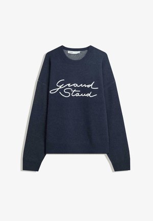 Dunkelblauer Pullover mit langen Ärmeln und gerippten Bündchen. Mit weißem, geschwungenem Text "Grand Stand" auf der Vorderseite, aus weichem Strickmaterial.
