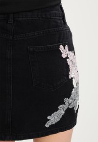 Černá džínsová sukně s květinovou výšivkou v růžové, bílé a šedé barvě na boku a zadní kapse, s přiléhavým střihem.