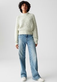 Maglione lavorato a maglia verde chiaro con texture a coste, abbinato a jeans a gamba larga blu chiaro e sneakers bianche.