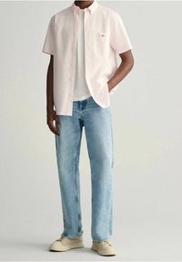 Camisa de botones de manga corta en rosa claro con patrón de cuadrícula, camiseta blanca de cuello redondo debajo, combinada con jeans rectos de color azul claro y zapatillas beige.