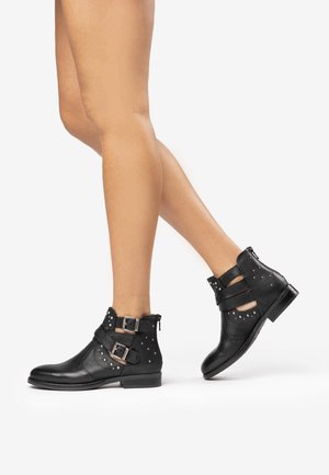Stivali alla caviglia in pelle nera con due fibbie, dettagli borchiati e tacco basso; presentano ritagli sui lati per una migliore traspirazione.