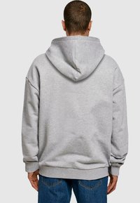 Sweat à capuche gris, à la coupe ample et avec des poignets côtelés, présentant une texture lisse et une poche kangourou à l'avant.