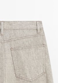 Hellegraue Denim-Jeans mit hoher Taille, Gesäßtasche und subtilen Nähdetails. Der Stoff hat eine strukturierte Oberfläche.
