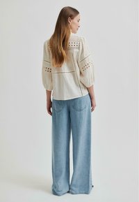 Cremfarbene, strukturierte Bluse mit Lochmuster und Ballonärmeln, kombiniert mit hellblauen weiten Jeans. Einfaches, entspanntes Design.