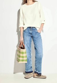 Top bianco a costine con maniche 3/4, jeans azzurri chiari, scarpe slip-on color beige e una borsa a tracolla a quadri verdi con manici in pelle marrone.
