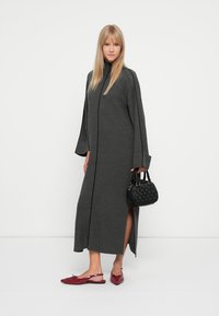 Gray knitted coat with long sleeves and side slits, paired with red flat shoes and a textured black handbag. Simple, structured design.