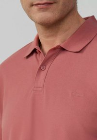 Kurzarm-Polohemd in staubigem Rosé, aus strukturiertem Stoff. Verfügt über einen klassischen Kragen, eine Zwei-Knopf-Leiste und ein dezentes Logo auf der Brust.