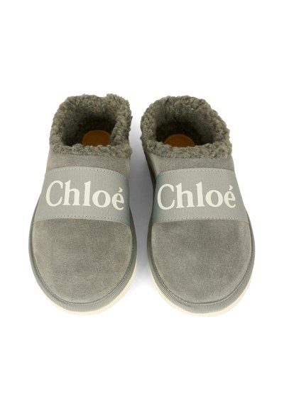 Chaussons en suede gris à enfiler avec doublure en peau de mouton, dotés de larges bandes élastiques sur le dessus, chacune imprimée du logo "Chloé" en blanc.