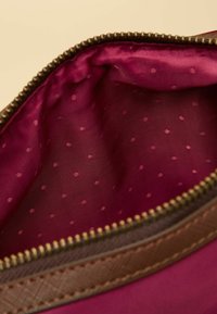 Wnętrze saszetki w kolorze bordowym o gładkiej fakturze z drobnymi różowymi groszkami, obramowane brązowym zamkiem błyskawicznym i brązową lamówką.