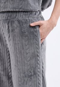 Szare dresowe spodnie z polaru o prążkowanej strukturze, z elastycznym paskiem w talii i boczną kieszenią, prezentujące miękką tkaninę i luźny krój.