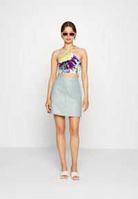 Top cropped halter colorido com padrão floral, emparelhado com uma mini saia de imitação de couro azul clara. Modelo usa óculos de sol cor-de-rosa e sandálias neutras.