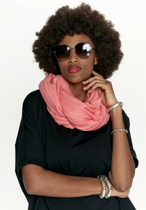 Koralowy szalik w nieskończoność, wykonany z lekkiego materiału. Modelka nosi oversize'owy czarny top i duże czarne okulary przeciwsłoneczne, uzupełniając stylizację srebrnymi bransoletkami.