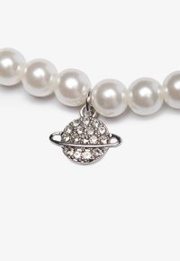 Collar de perlas con cuentas blancas brillantes, con un charm de planeta plateado adornado con strass transparentes y un acento de anillo intrincado.