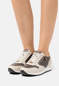 Baskets texturées avec un schéma de couleurs beige et marron, un motif décoratif, des accents dorés et une fermeture éclair sur le côté.