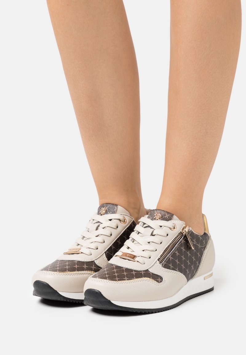 Baskets texturées avec un schéma de couleurs beige et marron, un motif décoratif, des accents dorés et une fermeture éclair sur le côté.