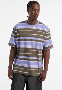 Gestreiftes T-Shirt in lila, olivgrün und weiß; lockere Passform mit kurzen Ärmeln und besticktem "Guess Originals"-Logo.