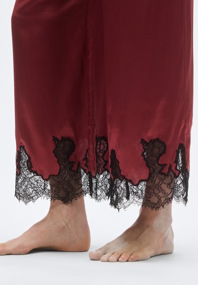 Czerwona satynowa nocna koszula z falistym czarnym koronkowym brzegiem. Koronka zdobiąca kwiatowe wzory kontrastuje z gładką tkaniną sukienki.