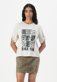 Beige short-sleeve t-shirt with a black and white animal print graphic and text "DREAM BIG" on the front, paired with a leopard print skirt.